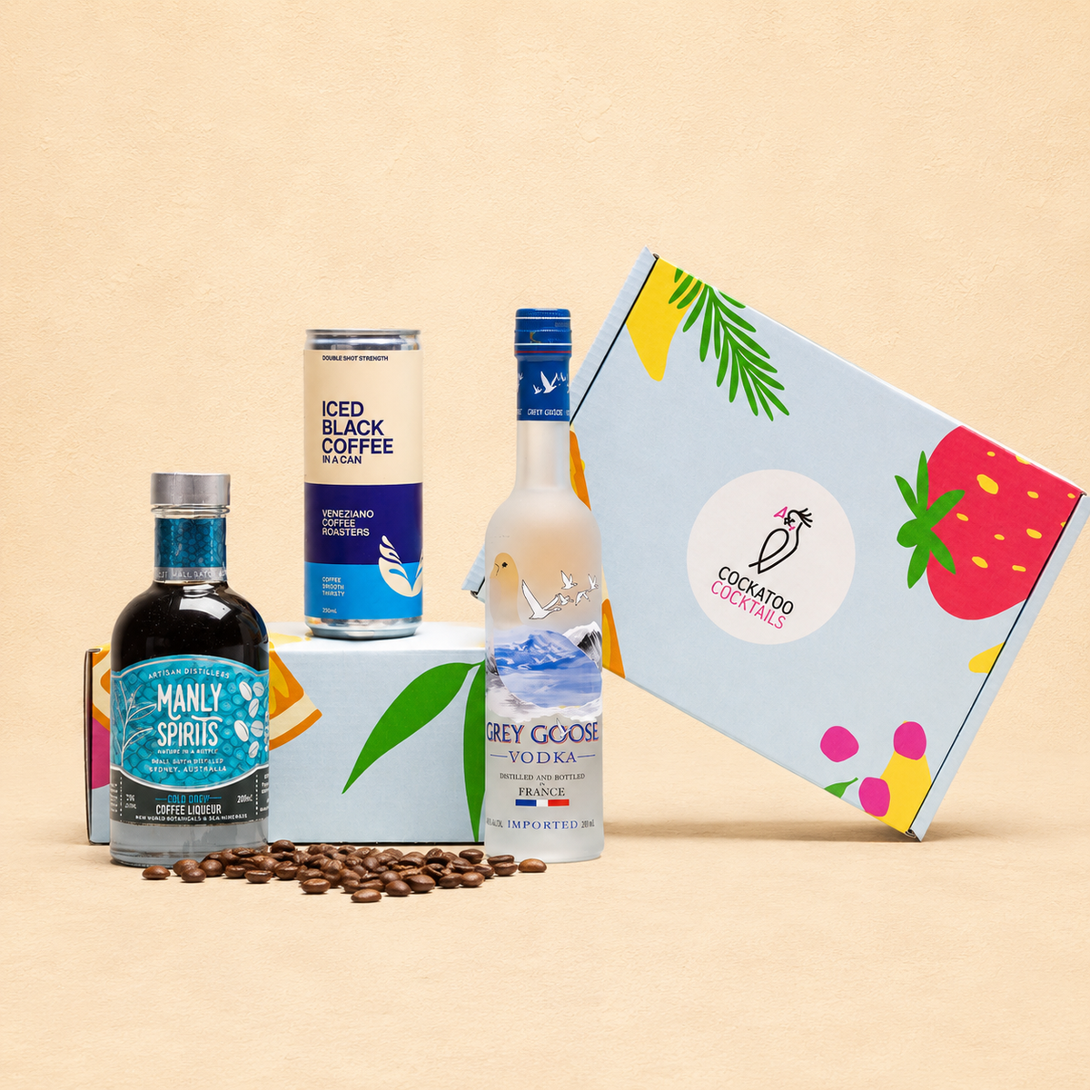 A Cockatoo Cocktails gift set featuring a bottle of Manly's Spirits, Cold Drip Coffee, and a Grey Goose Vodka bottle, arranged with coffee beans in front of a branded Cockatoo Cocktails gift box on a beige background.