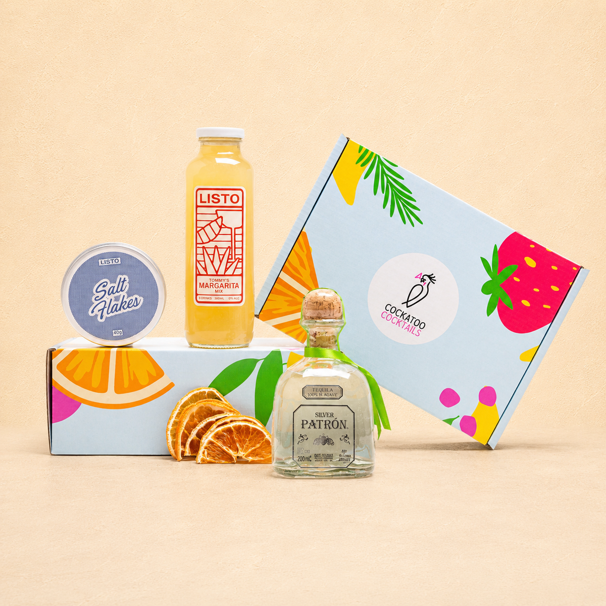 A curated gift set featuring a bottle of Listo Margarita , a bottle of Patrón tequila, a tin of Salt, and colorful illustrated gift box on a warm beige background.