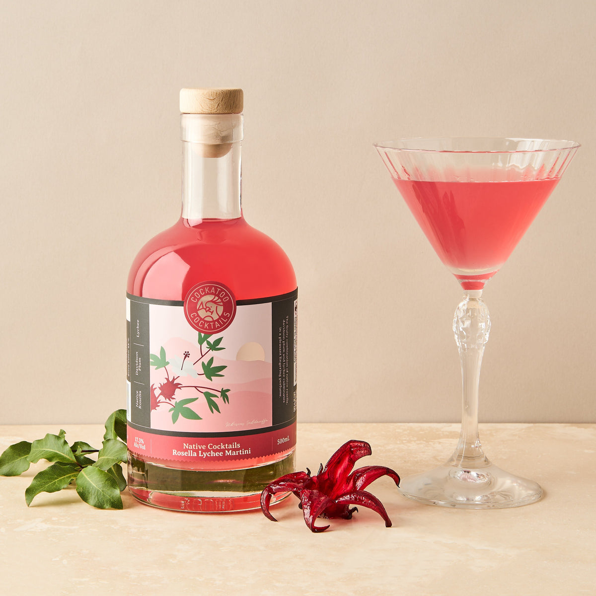 A bottle of Rosella Lychee Martini Cocktail with a glass of the cocktail and rosella fruit in the foreground.
